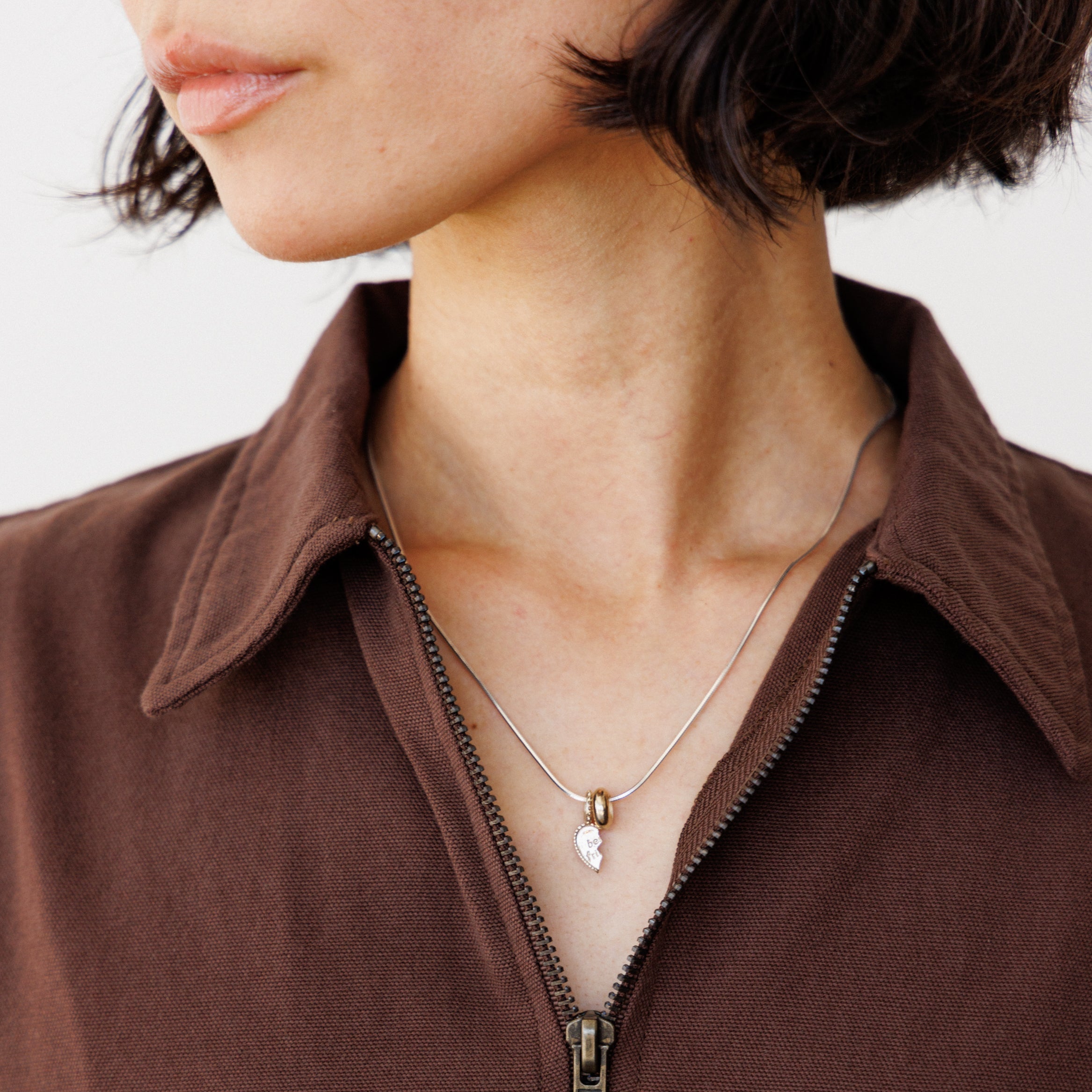 Close-up of a person wearing a brown dress with a necklace featuring a silver heart charm.