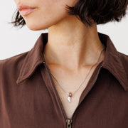 Close-up of a person wearing a brown dress with a necklace featuring a silver heart charm.