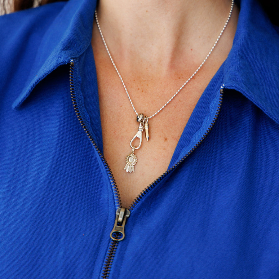 Close-up of a person wearing a silver necklace with charms against a blue jacket.