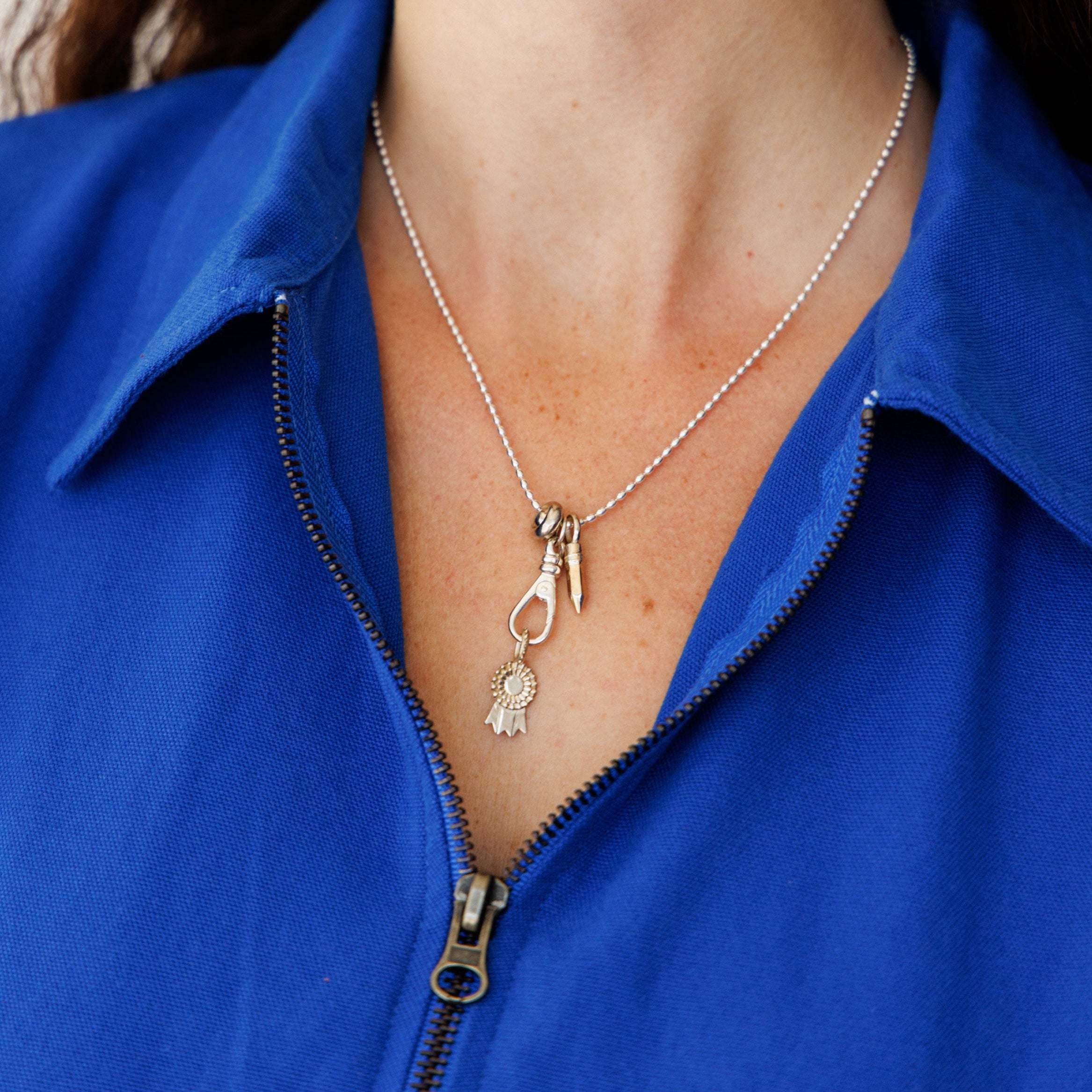 Close-up of a person wearing a silver necklace with a pendant against a blue jacket.