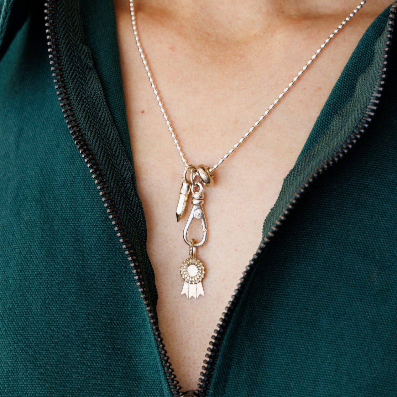 Person wearing a green zip-up dress with a silver charm jumble.