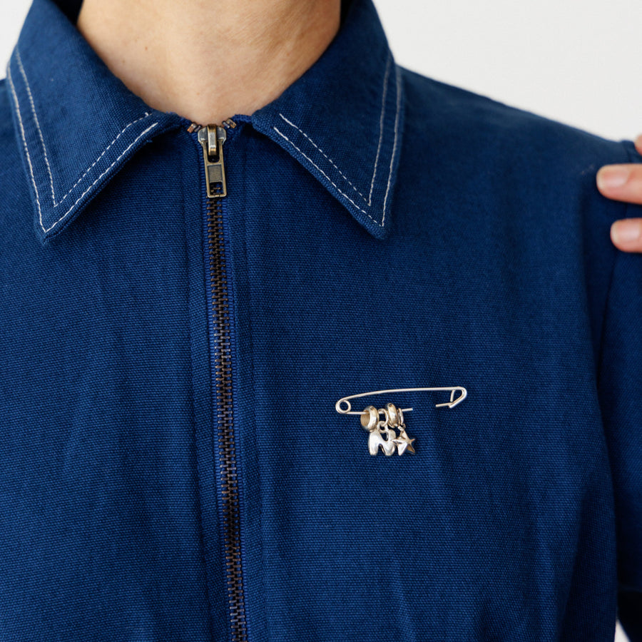 Person wearing a blue jacket with a safety pin brooch featuring silver initial charms.