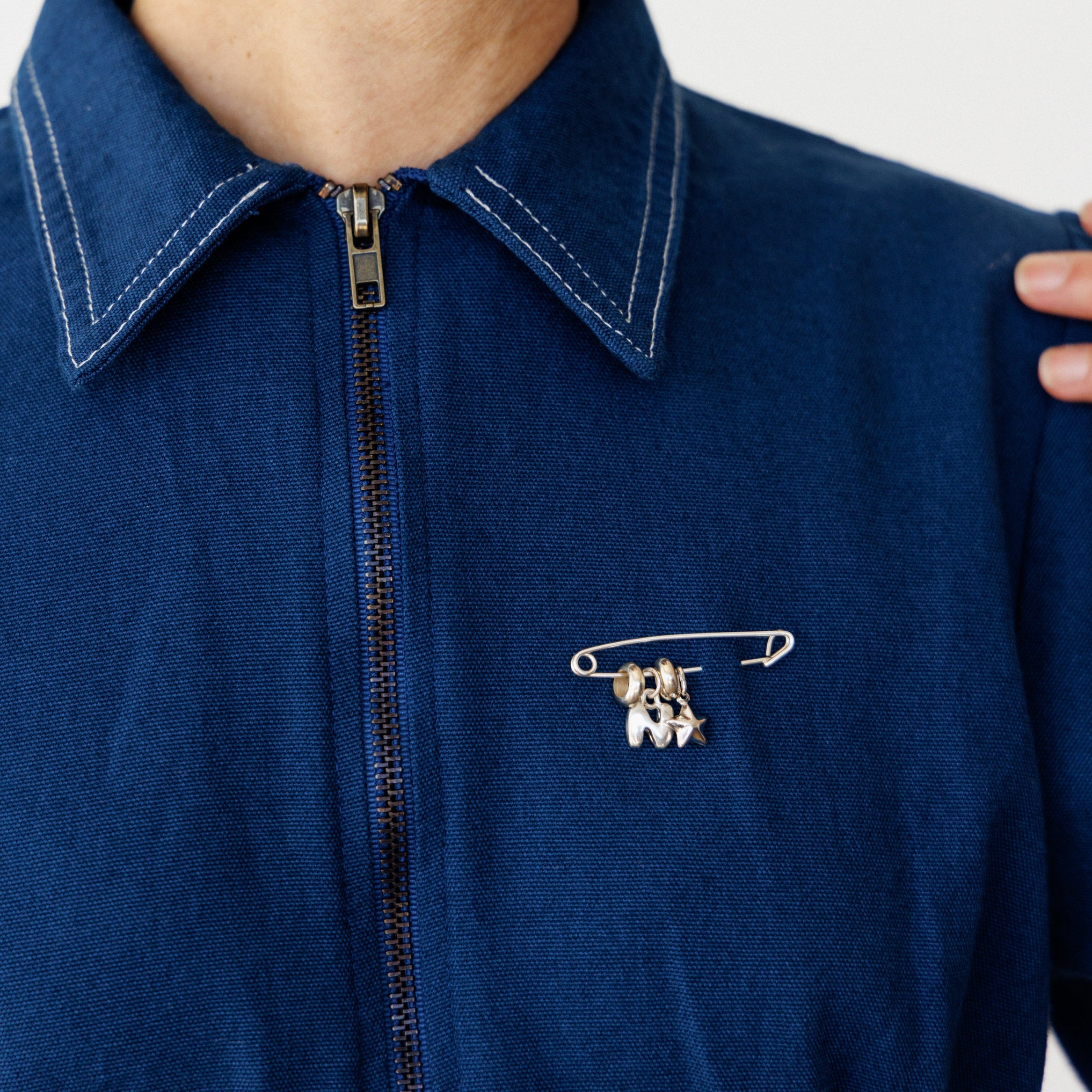 Person wearing a blue jacket with a safety pin brooch featuring silver charms.