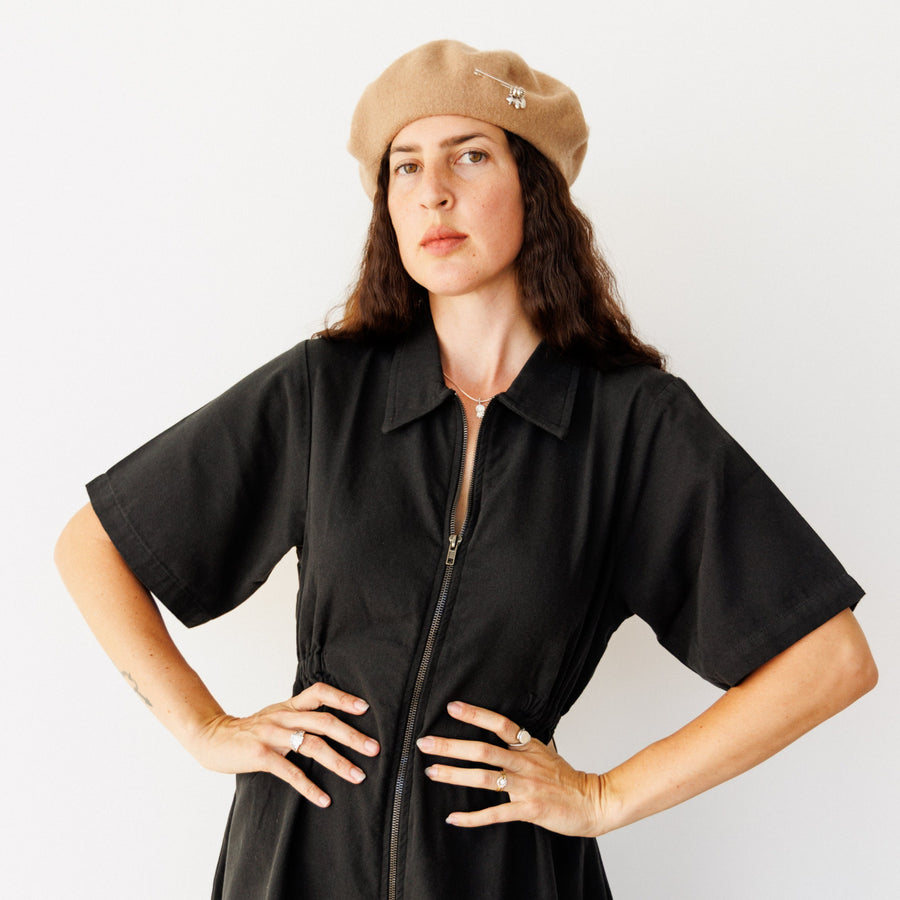 Woman wearing a black dress and beige beret against a white background