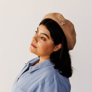 Woman wearing a blue shirt and brown hat with silver charms on the hat.