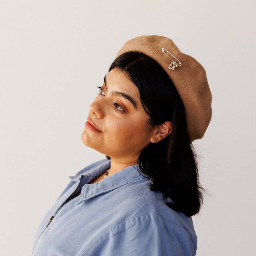 Woman wearing a blue shirt and brown hat with silver charms on the hat.