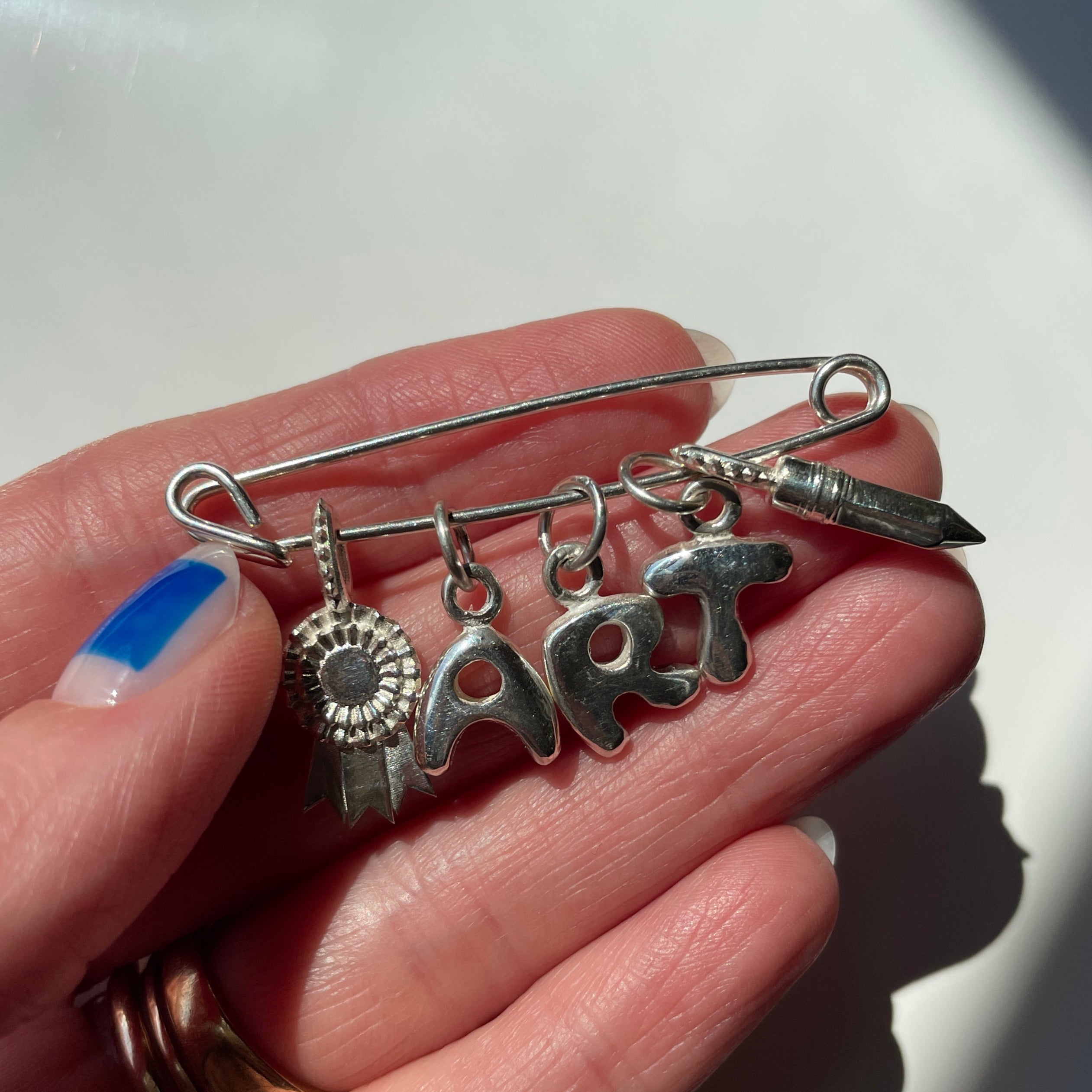 Silver brooch with charms held by a hand on a white background