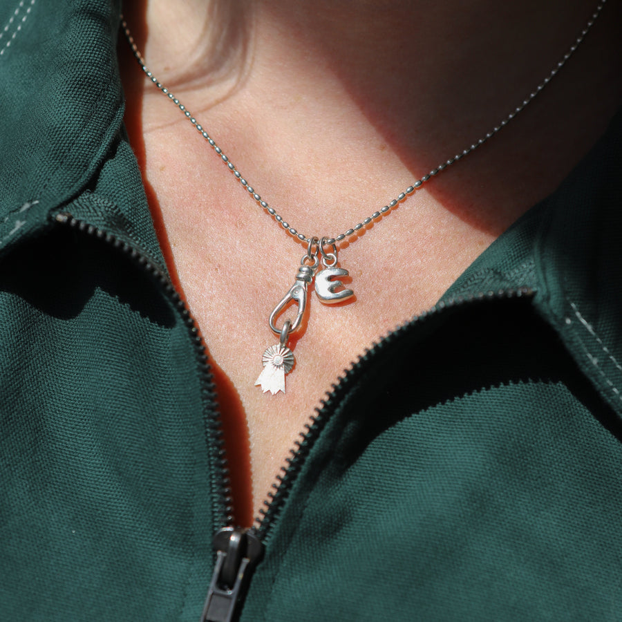 Close-up of a person wearing a green dress with a necklace featuring a 'E' and award pendant.