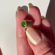 Hand holding charm with a green gemstone on a neutral background
