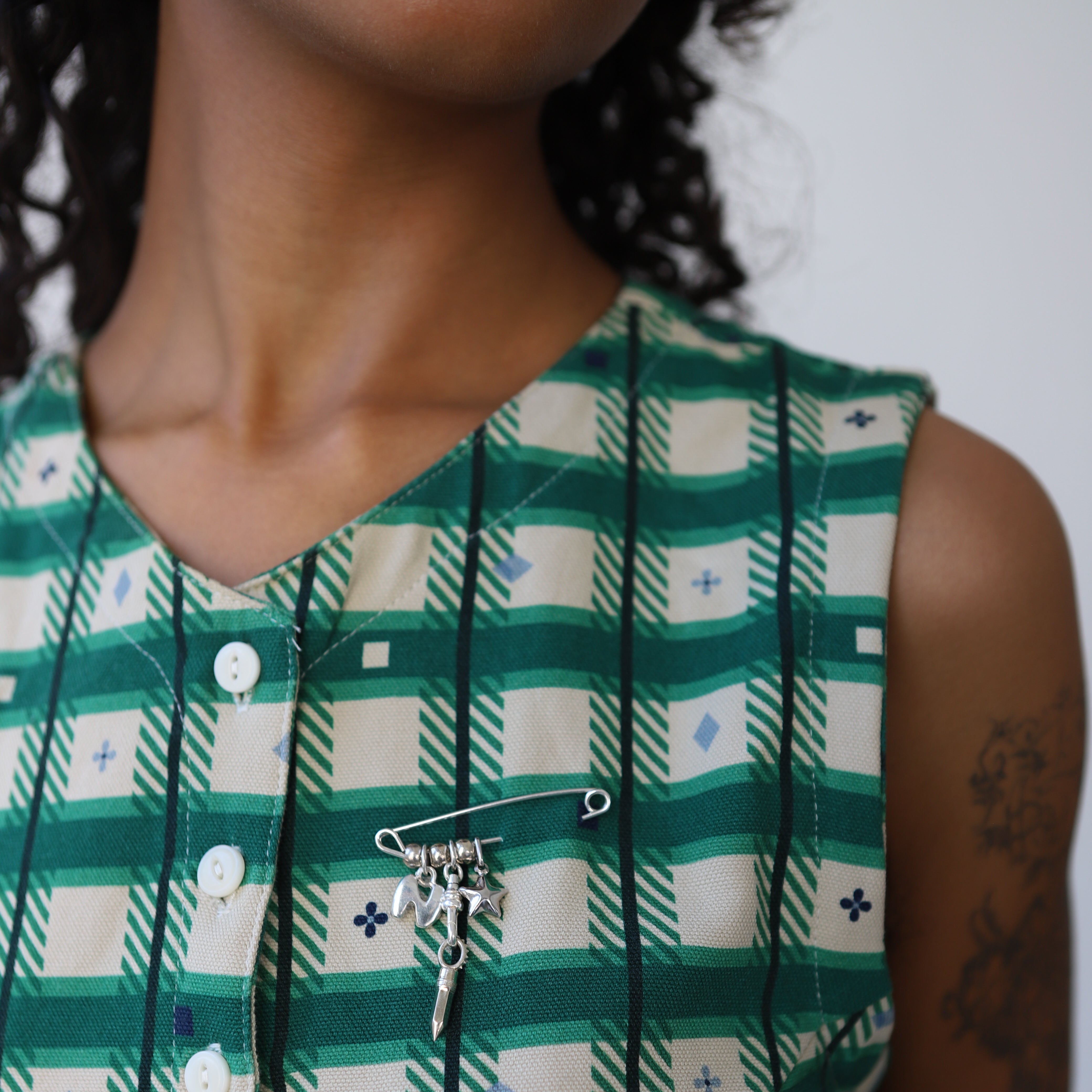 Person wearing a green and white checkered dress with a silver pin with charms.