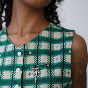 Person wearing a green and white checkered dress with a silver pin with charms.