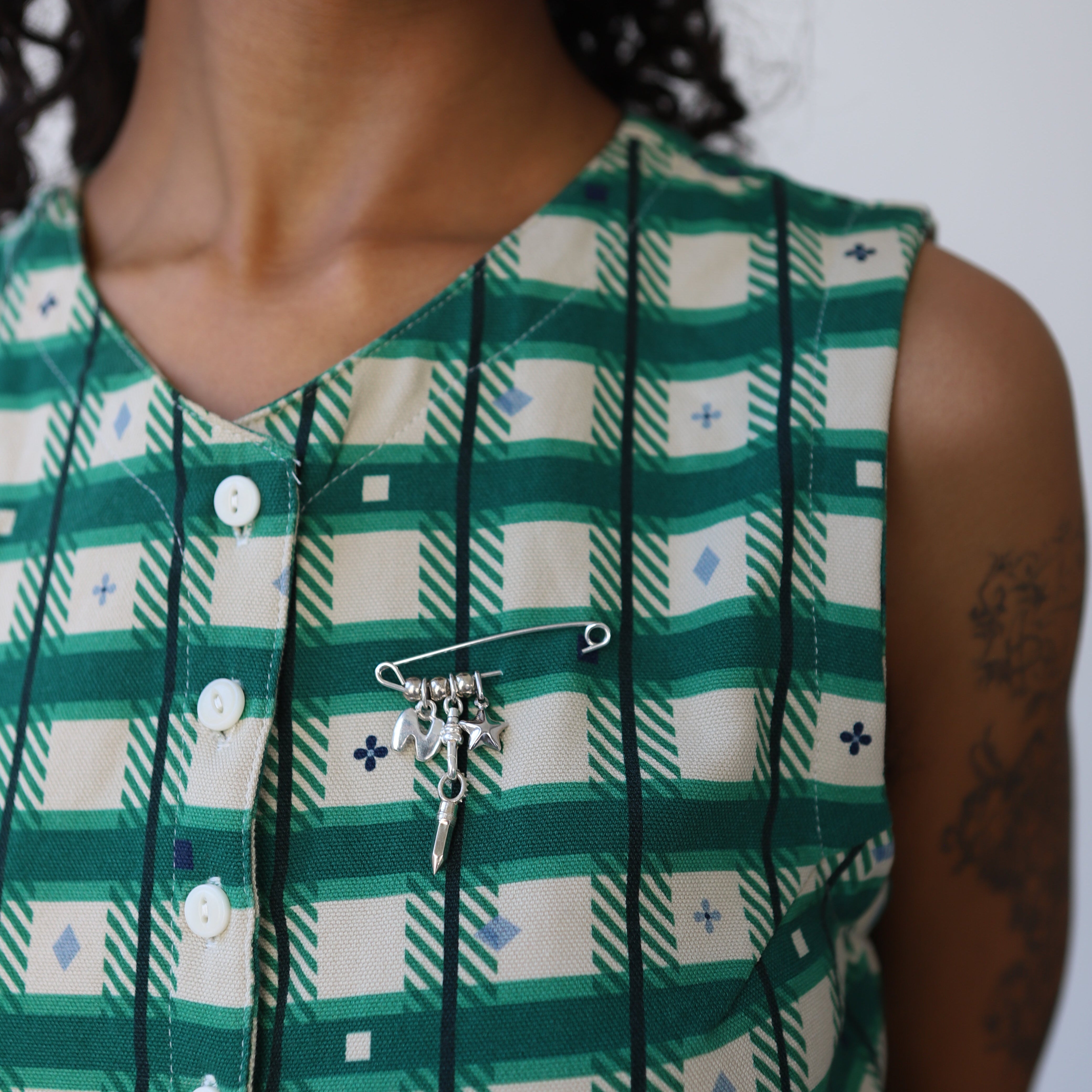 Person wearing a green and white checkered dress with a silver safety pin with silver charms.