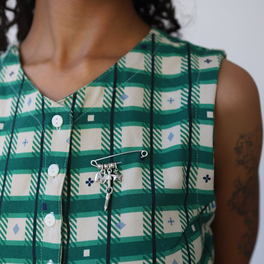 Person wearing a green and white checkered dress with a silver safety pin with silver charms.