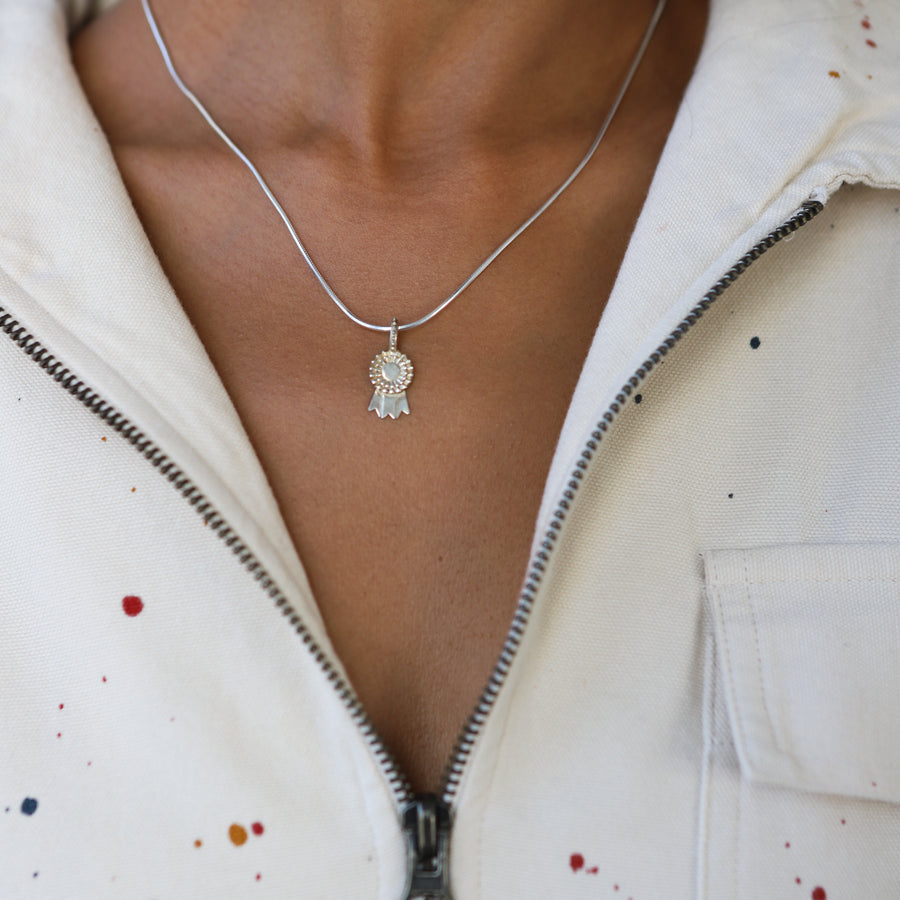 Necklace with a pendant worn by a person in a white jacket with colorful speckles.