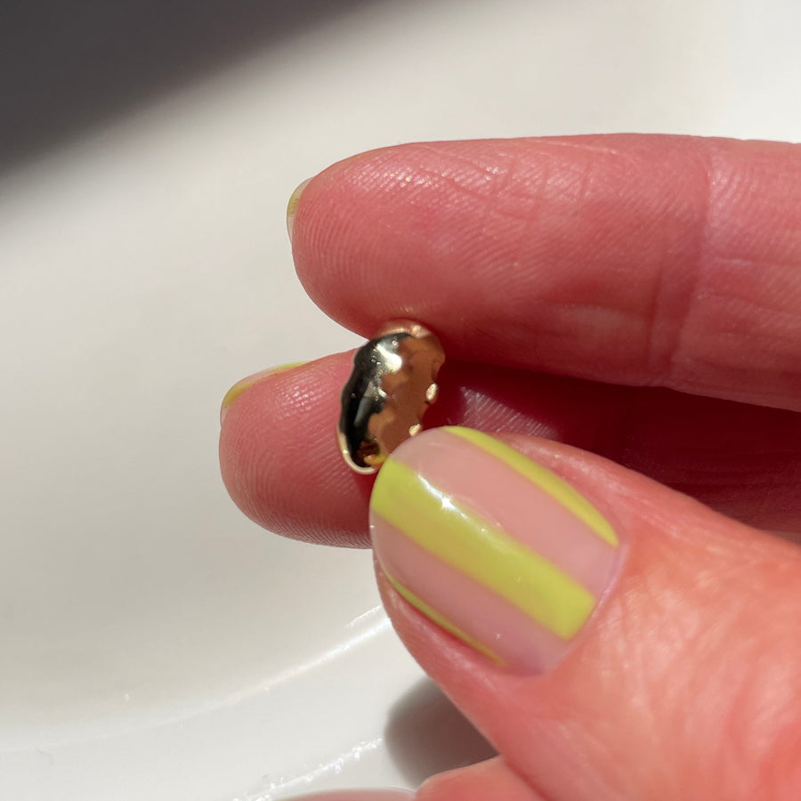 Close-up of a hand with yellow and pink striped nail polish holding a small gold bead.