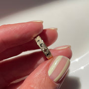 Hand holding a gold ring with intricate design on a white background