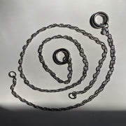A dark sterling silver chain necklace with a circular ring clasp, coiled on a light gray surface with a strong shadow.