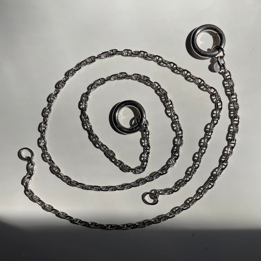 A dark sterling silver chain necklace with a circular ring clasp, coiled on a light gray surface with a strong shadow.