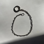 A sterling silver metal chain bracelet with a textured, rope-like link pattern and a circular ring charm, displayed on a reflective gray surface.