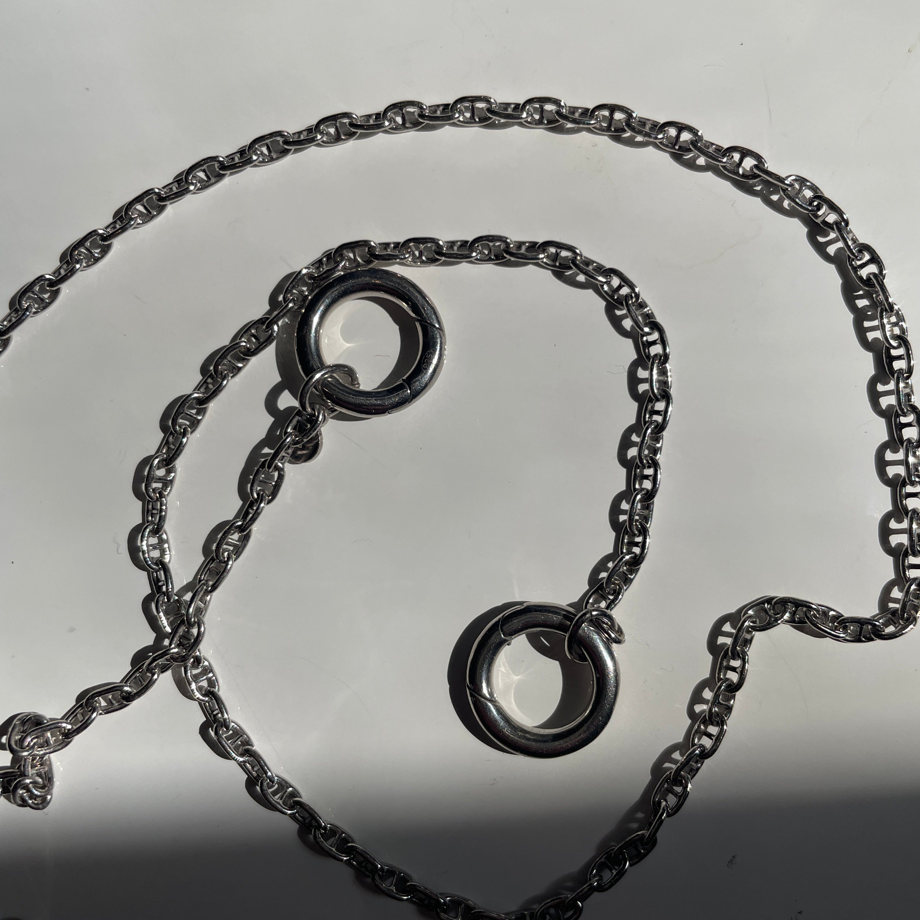 A sterling silver necklace with two interlocking circular ring charms, displayed on a light gray surface.