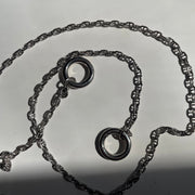 A sterling silver necklace with two interlocking circular ring charms, displayed on a light gray surface.