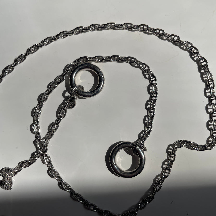 A sterling silver necklace with two interlocking circular ring charms, displayed on a light gray surface.