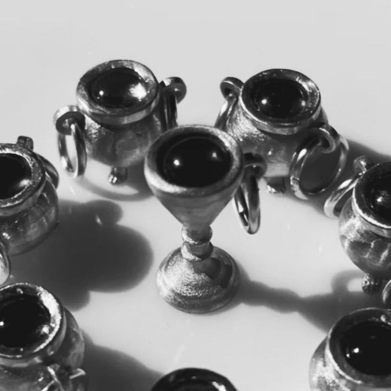 A close-up of several small silver cup charms arranged in a circle on a light background, photographed in monochrome.
